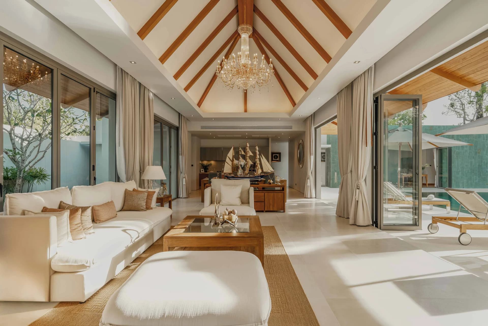 Living room of a built Anchan 4C: timber rafters, a chandelier and glass doors to the pool